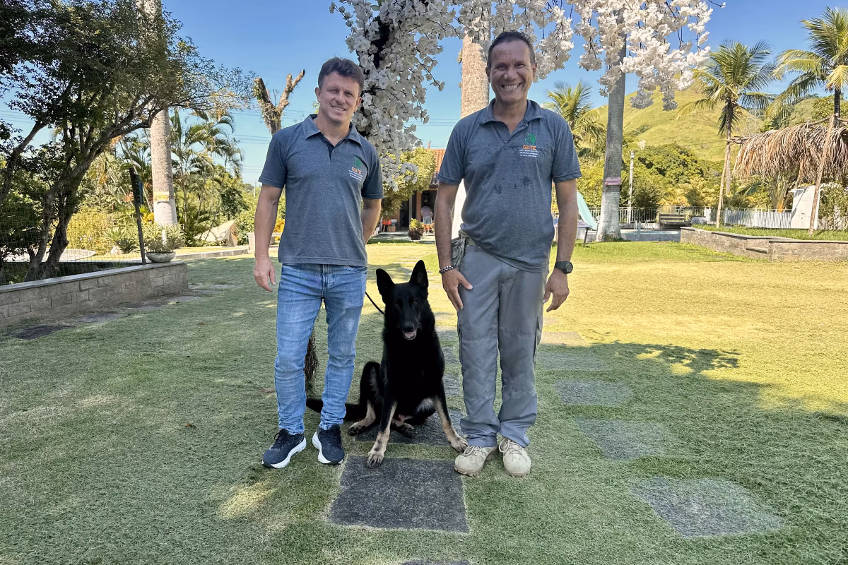 Leishmaniose canina: sintomas, tratamento e prevenção Cão preto sentado entre dois integrantes da equipe do Gute no jardim